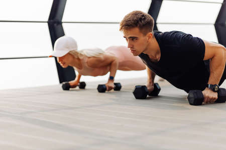 Young couple exercising outdoors, Attractive sportive woman and handsome muscular man are exercising on the bridge on the coast, Doing plank on kettlebell, doing push-ups, Sport concept, motivationの写真素材