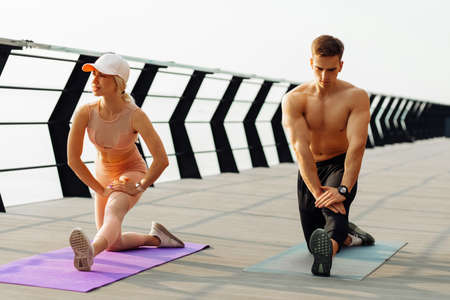 Young fitness couple in sportswear doing morning workout outdoors on the pier, Young man and woman stretching muscles before running across the bridgeの写真素材