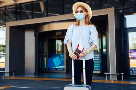 Young woman holding passport and tickets, wearing a protective mask in the city, Woman with a suitcase, Business travel during a pandemic, protection from virus, healthy lifestyle, tourism conceptの写真素材