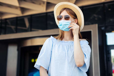 Young woman holding passport and tickets, wearing a protective mask in the city, Woman with a suitcase, Business travel during a pandemic, protection from corona virus, healthy lifestyle, tourism conceptの写真素材