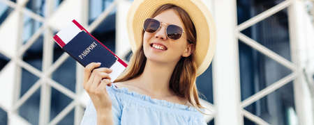 Smiling young woman in summer hat and glasses, traveler with passport in hands and plane tickets,...