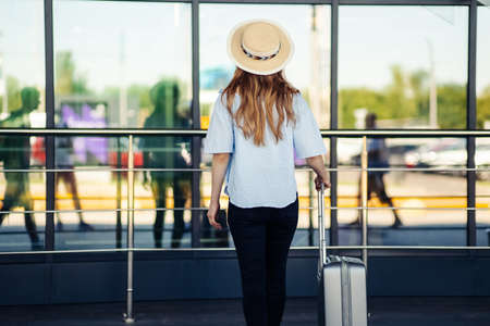 Woman traveler with luggage at international airport, woman at airport window looking through airport gate windows in planes on airport runway, travel, tourismの写真素材