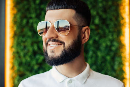 Portrait of a happy young man with a beard, in a white shirt and sunglasses, against a background of...