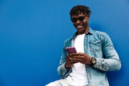 african man typing sms on blue background, 5g internet concept, high speed internet on phone, black...