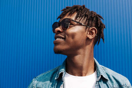 portrait of an african guy in sunglasses, on a blue background, black guy model, looking to the sideの写真素材
