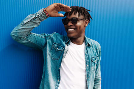 african guy looks at the sun, against the background of a blue building in the city, concept: striving for successの写真素材