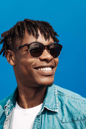 african man in sunglasses stands against a blue wall of a building in the city, handsome black man smilingの写真素材