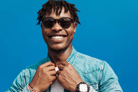 african man in sunglasses stands against a blue wall of a building in the city, handsome black man smilingの写真素材