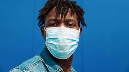 portrait of an afro american black man wearing a protective mask from the coronavirus, blue backgroundの写真素材