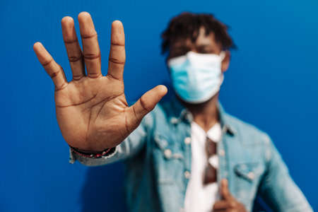 portrait of afro american black man wearing protective mask from coronavirus, making stop coronavirus hand gesture, concept: protest against coronavirusの写真素材