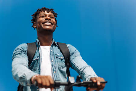 modern african american on electric scooter, business man is one to work, student is one to study, against the background of a blue buildingの写真素材
