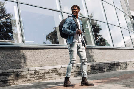 a dark-skinned African American with a laptop in his hands walks down the street against a stele building, in the city centerの写真素材