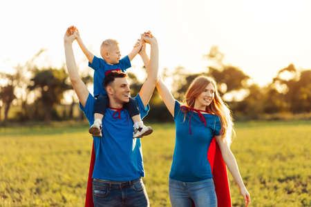 concept of european superfamily, outdoors, loving father holds on the neck, superhero family run at sunset in nature, happy family travelの写真素材