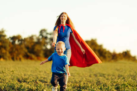 concept of super mom with baby, mom with super hero cloak runs after baby, outdoors, in nature at sunsetの写真素材