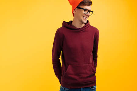 portrait of a handsome guy in an orange hat, red sweater and glasses, on a yellow background,...