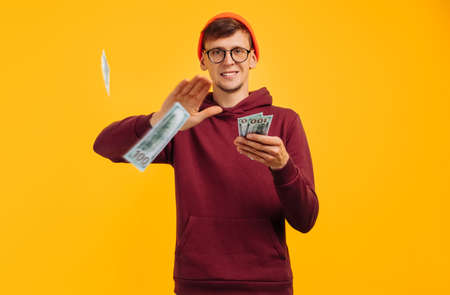 handsome guy in an orange hat with glasses and red sweatshirt, throws one dollar bill, concept: a...