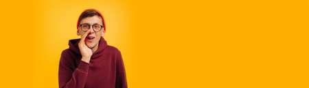 handsome guy says something in secret, a guy in an orange hat and a red sweater is gossiping, talking in gray, on a yellow backgroundの写真素材