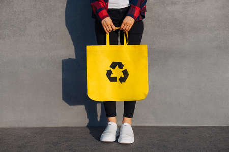 Young woman holding shopping bag with recycling symbol, Ecological recycling concept, reuse, Woman in city on urban gray isolated wall backgroundの写真素材