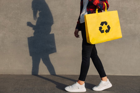 Young woman walking with shopping bag with recycling symbol, Ecological concept of recycling reduction, reuse, Woman walking in city on urban gray isolated wall backgroundの写真素材