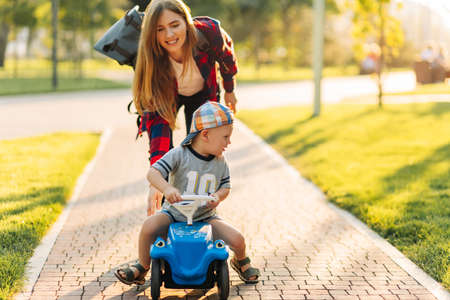 Happy cute boy ride a child's car, walking in the park with mom, mom teaches her son to ride a car in the park on a summer dayの写真素材