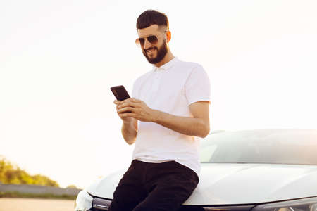 Handsome young man with smartphone near modern car outdoors, Handsome man on background of carの写真素材