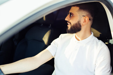 Happy young man, wearing sunglasses, sits in the driver's seat and smiles, Taxi driver listens to music in the car and drivesの写真素材