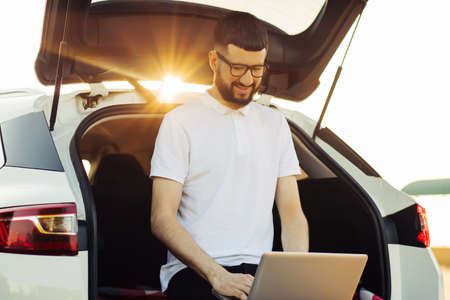 Young business man using a laptop laptop to work in the trunk of a car, enjoying the trip, travel and weekend adventuresの写真素材