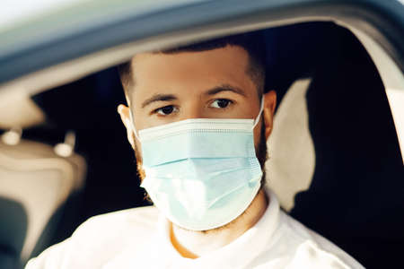 Young man in protective sterile medical mask driving a car, Concept of preventing the spread of the epidemic and treating the coronavirus pandemic, COVID-19の写真素材