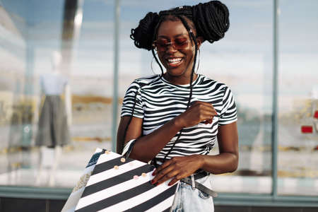 Happy beautiful young African American woman wearing black glasses, with black shopping bags, Black Friday, sale, fashion, peopleの写真素材
