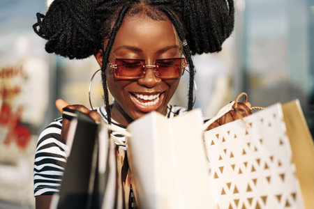 Excited happy African American curly woman enjoying shopping while standing on the street near shopping mall with shopping bags, Shopping, Black Fridayの写真素材