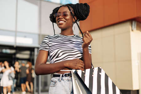 Portrait of a carefree fashionable African American woman wearing glasses, with shopping bags, happy woman with bags coming out of the store, shopping, Black Friday, salesの写真素材