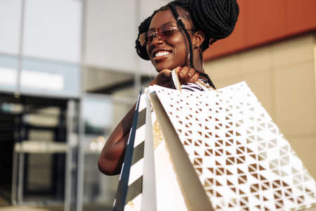 Portrait of a carefree fashionable African American woman wearing glasses, with shopping bags, happy woman with bags coming out of the store, shopping, Black Friday, salesの写真素材