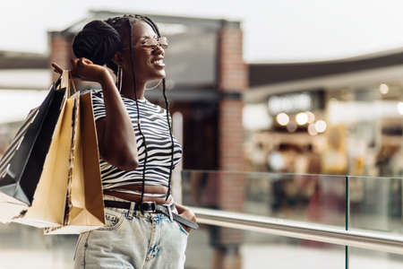 Young African American beautiful woman, with shopping bags walking in the mall, consumerism,...