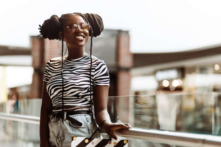 Portrait of smiling young black woman, wearing glasses, holding shopping bags, shopping mall, shopping concept, consumerismの写真素材