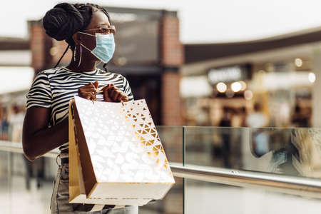 Young african american woman wearing protective mask at mall, woman with shopping bags shopping, shopping concept, quarantine, COVID-19の写真素材