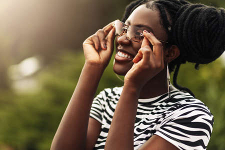 Portrait of young beautiful happy african american woman with hairstyle and sunglasses walking in city, smiling black woman outdoors in parkの写真素材