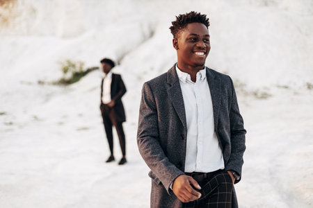 Two fashion models posing in the street, in classic clothes, suit, coat, fashionable African male models, in nature on the background of rocksの写真素材