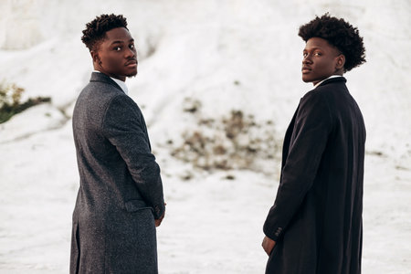 Two fashion models posing in the street, in classic clothes, suit, coat, fashionable African male models, in nature on the background of rocksの写真素材
