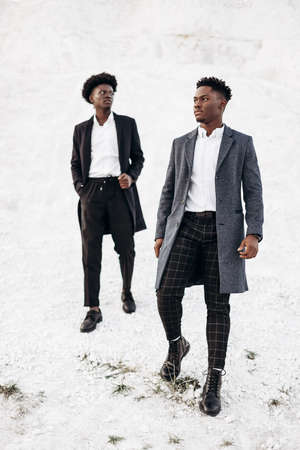 Two handsome African black men, walking and posing in classic clothes, down the street in fashionable coats, at sunset against the backdrop of white chalk mountainsの写真素材