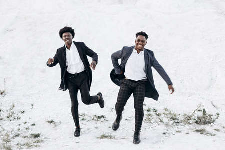 Fashionable Afro American curly haired men, in stylish identical suits, fashion posing in nature on a rocky area at sunsetの写真素材
