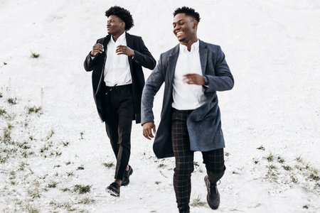 Fashionable Afro American curly haired men, in stylish identical suits, fashion posing in nature on a rocky area at sunsetの写真素材