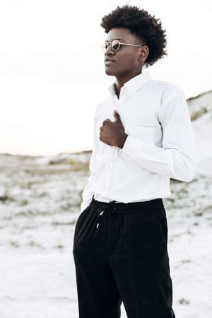 handsome African American man, with a curly hairstyle, in a white classic shirt and trousers, posing...