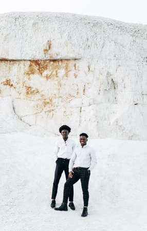 Two stylish handsome African American men. in black glasses and white elegant shirts, models posing outdoors against the backdrop of mountains in a rocky area.の写真素材