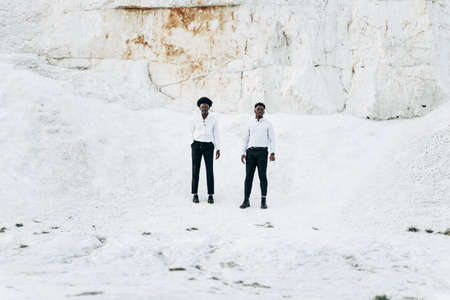 Two fashionable elegant black Africans, in white shirts, posing in full growth, outdoors near mountains and rocks, fashion posing with a beautiful landscape on the background, Fashion posing concept,の写真素材