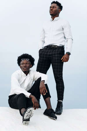 Two African American men, standing on the top of the mountain, climbing the rocks, businessman success, hiking on the peak of the mountain, winner leader conceptの写真素材