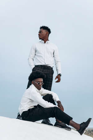 Two African American men, standing on the top of the mountain, climbing the rocks, businessman success, hiking on the peak of the mountain, winner leader conceptの写真素材