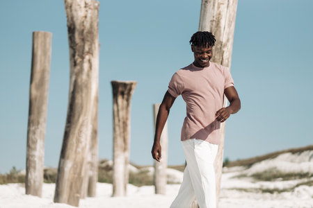 Cheerful smiling stylish African, man in pink T-shirt and white pants, African American model guy, walking in dry desert, Fashion concept, people, Wild West styleの写真素材
