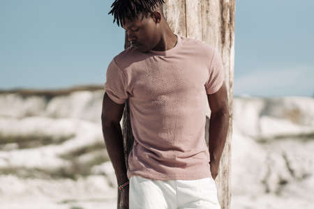 Open full length portrait of stylish handsome man, in stylish clothes, black man posing on sand,...