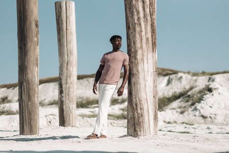 Open full length portrait of fashionable african black man wearing t-shirt and white pants walking in the desert at sunset, copy, blank space for textの写真素材