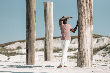 Open full length portrait of fashionable african black man wearing t-shirt and white pants walking in the desert at sunset, copy, blank space for textの写真素材